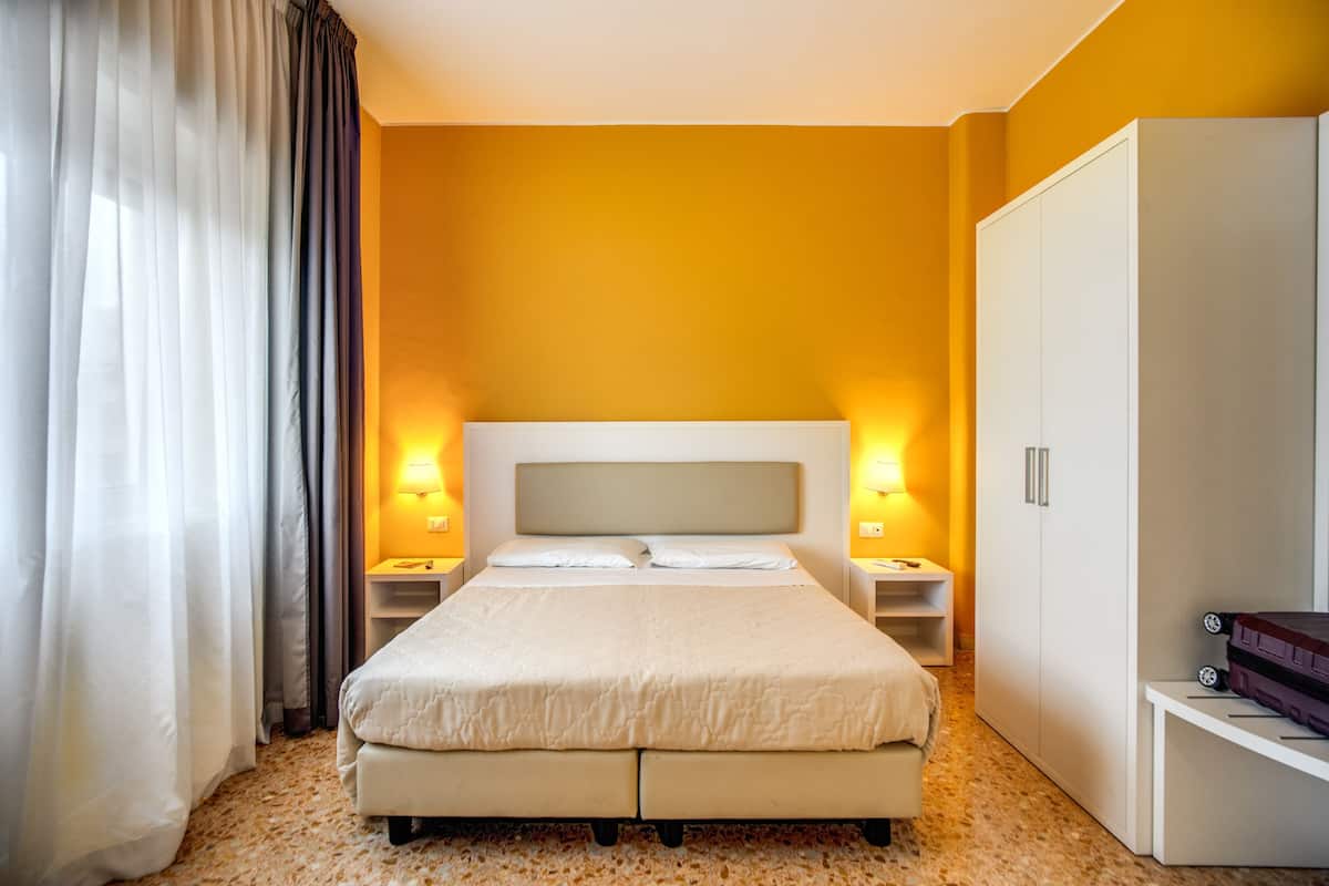 A hotel room with a large bed, two bedside tables with lamps, a wardrobe, and a suitcase on the floor.