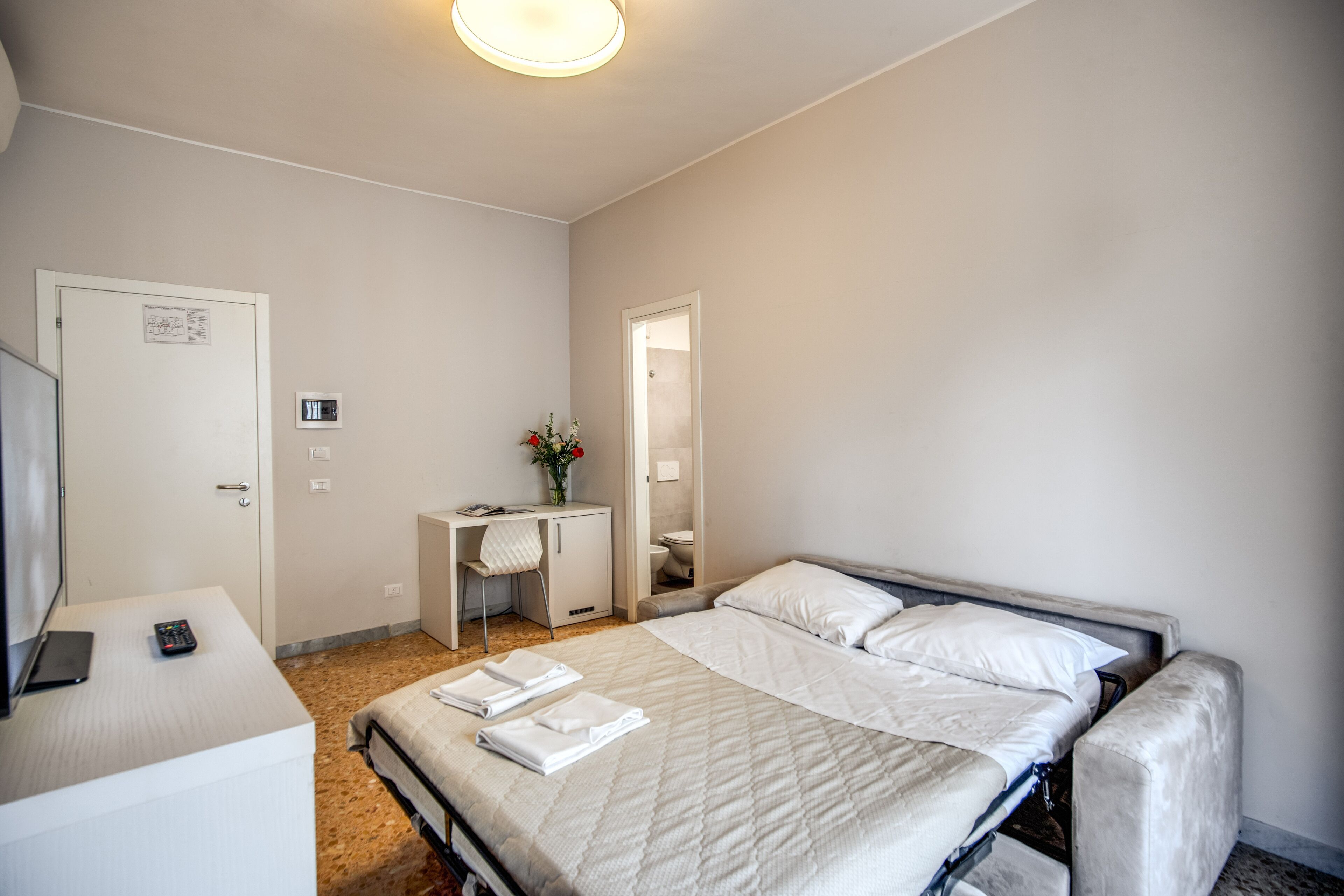 A hotel room with a bed, a desk, a chair, and a small bathroom.