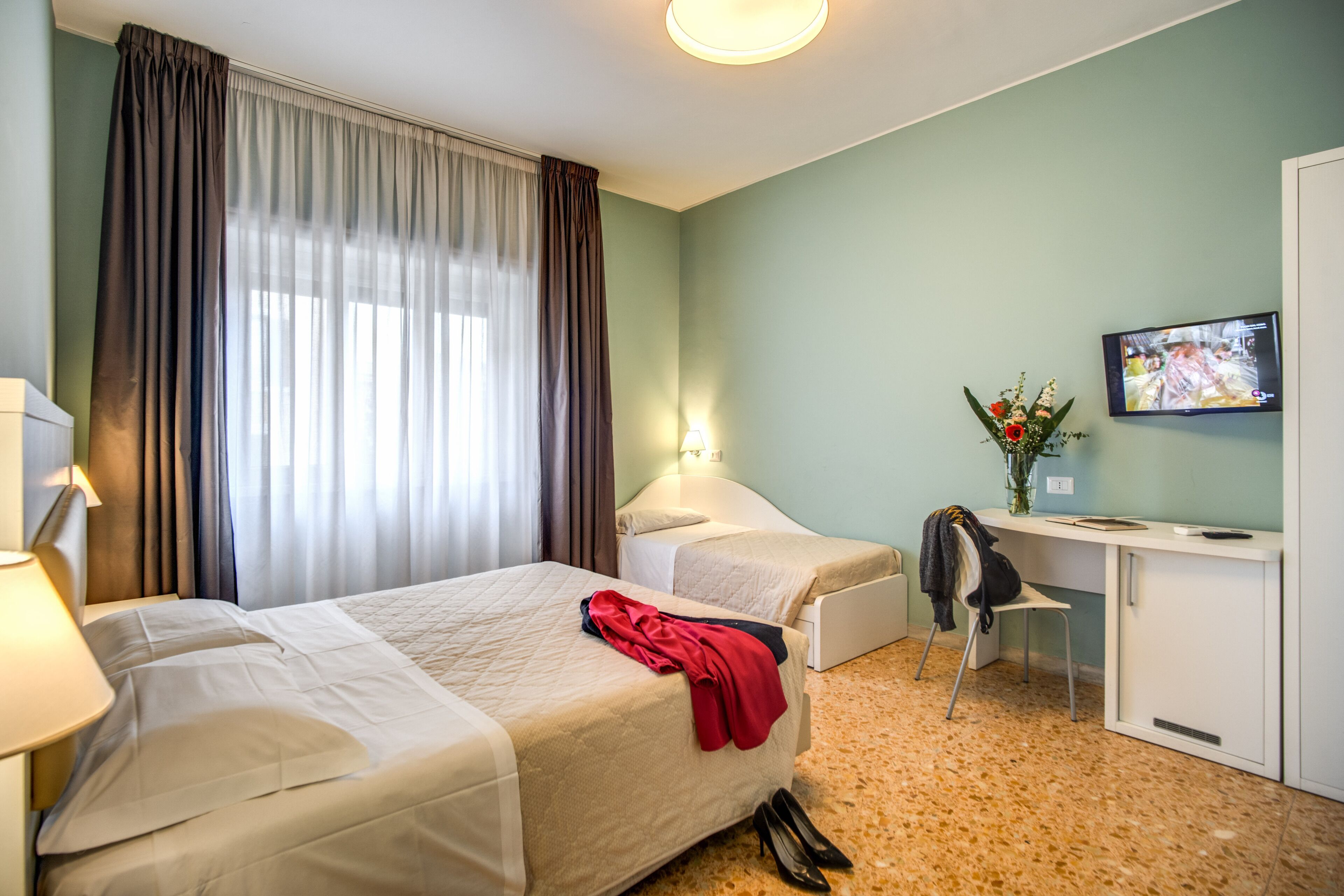 A hotel room with two beds, a desk, a chair, a TV, and a window with curtains.