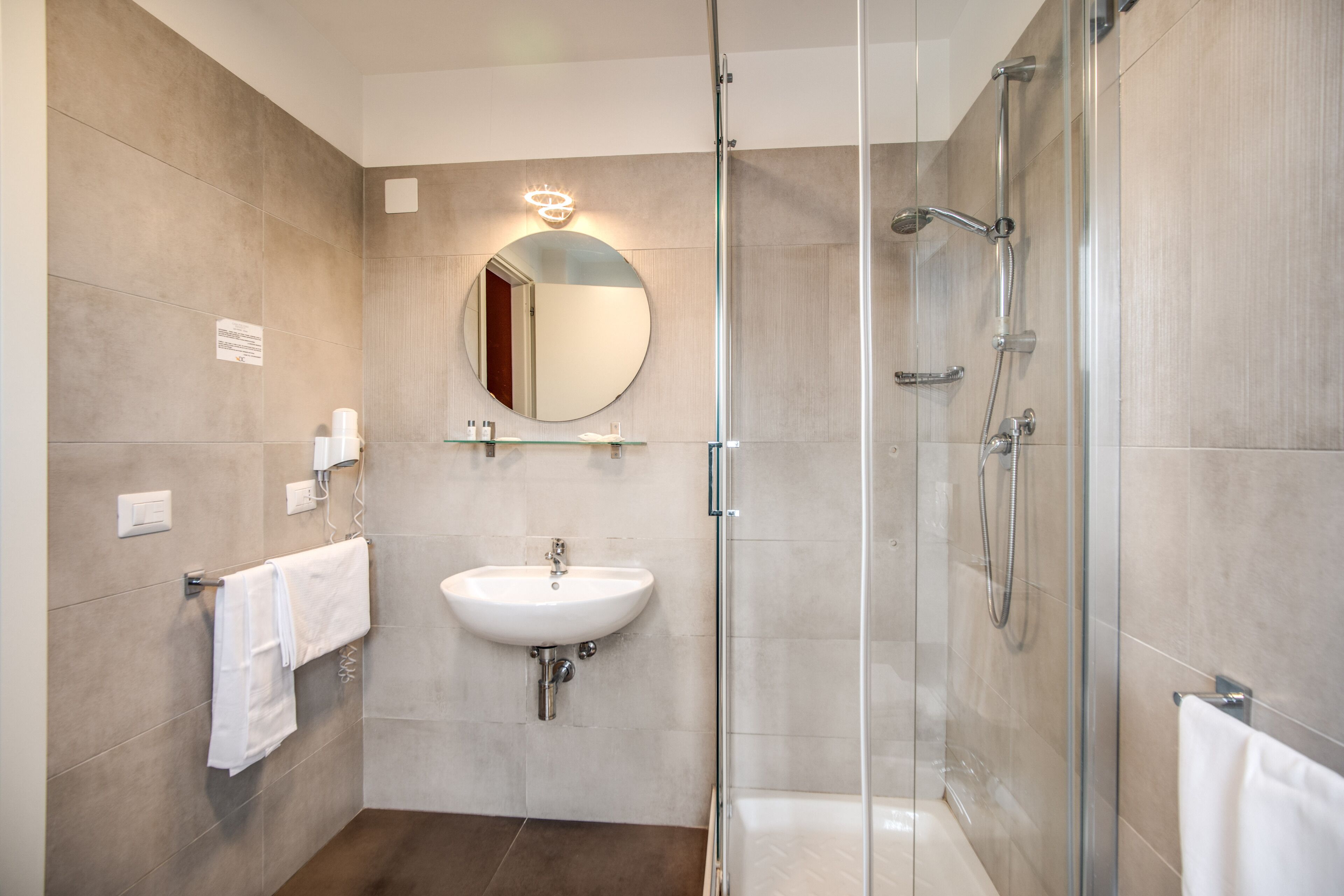Een moderne badkamer met een douche met glazen wand, een witte wastafel en een grote spiegel met een lamp erboven.