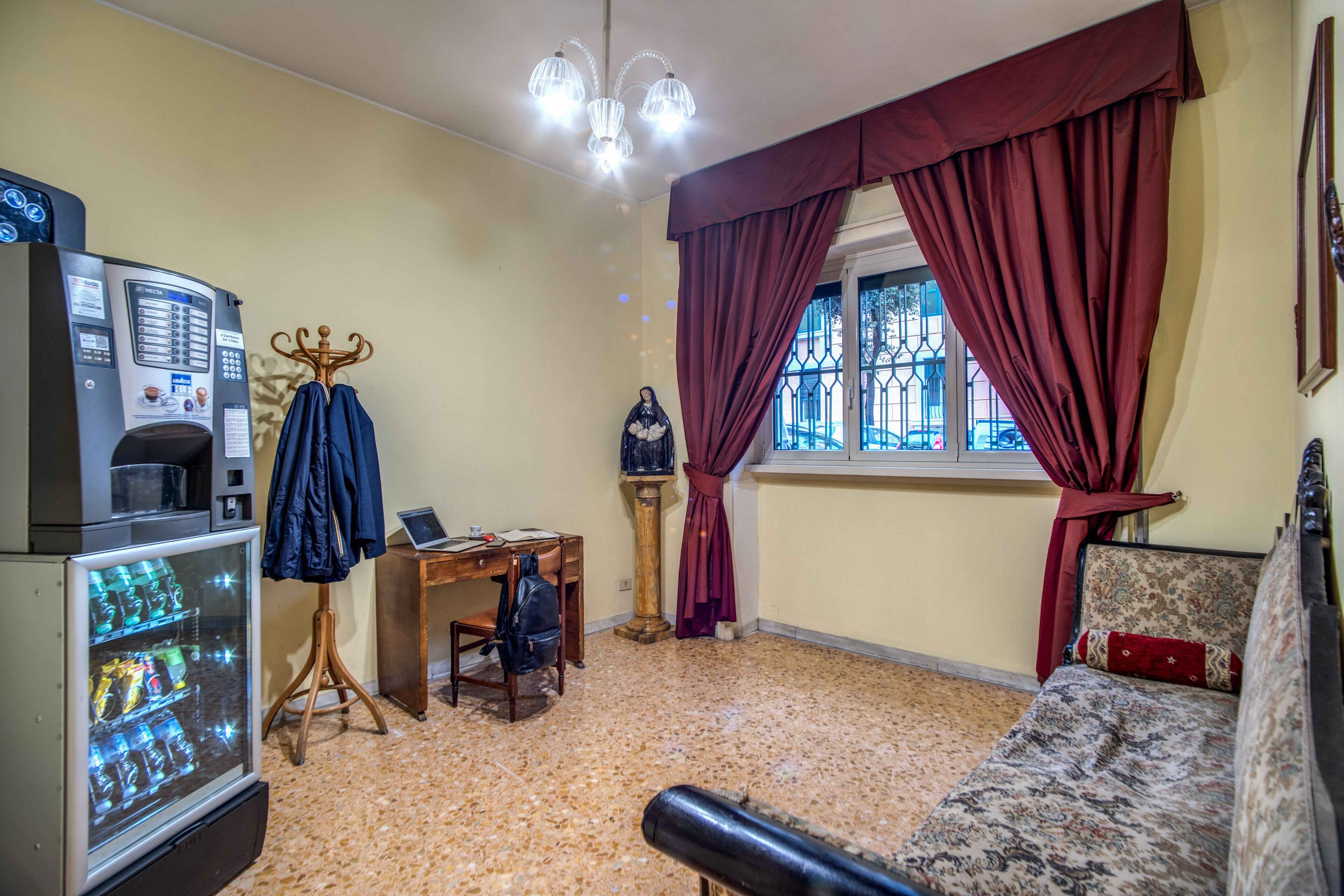 A room with a vending machine, a desk, a chair, a statue, a sofa, and a window with curtains.