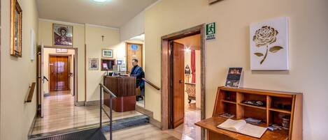 A hotel lobby with a reception desk, a staircase, and a wooden display cabinet.