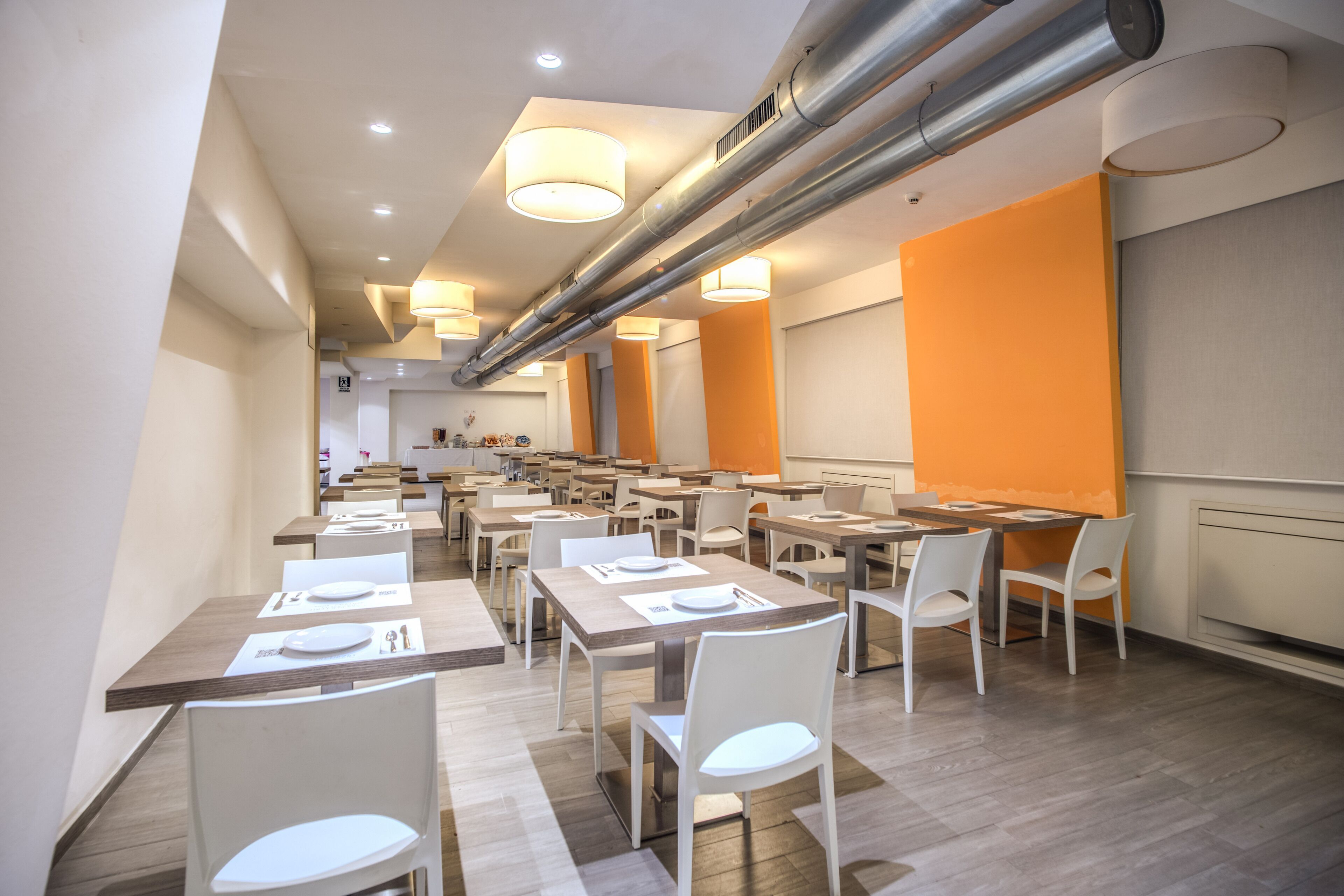 Un comedor moderno con sillas y mesas blancas, una barra de servicio central y paredes de acento naranja.