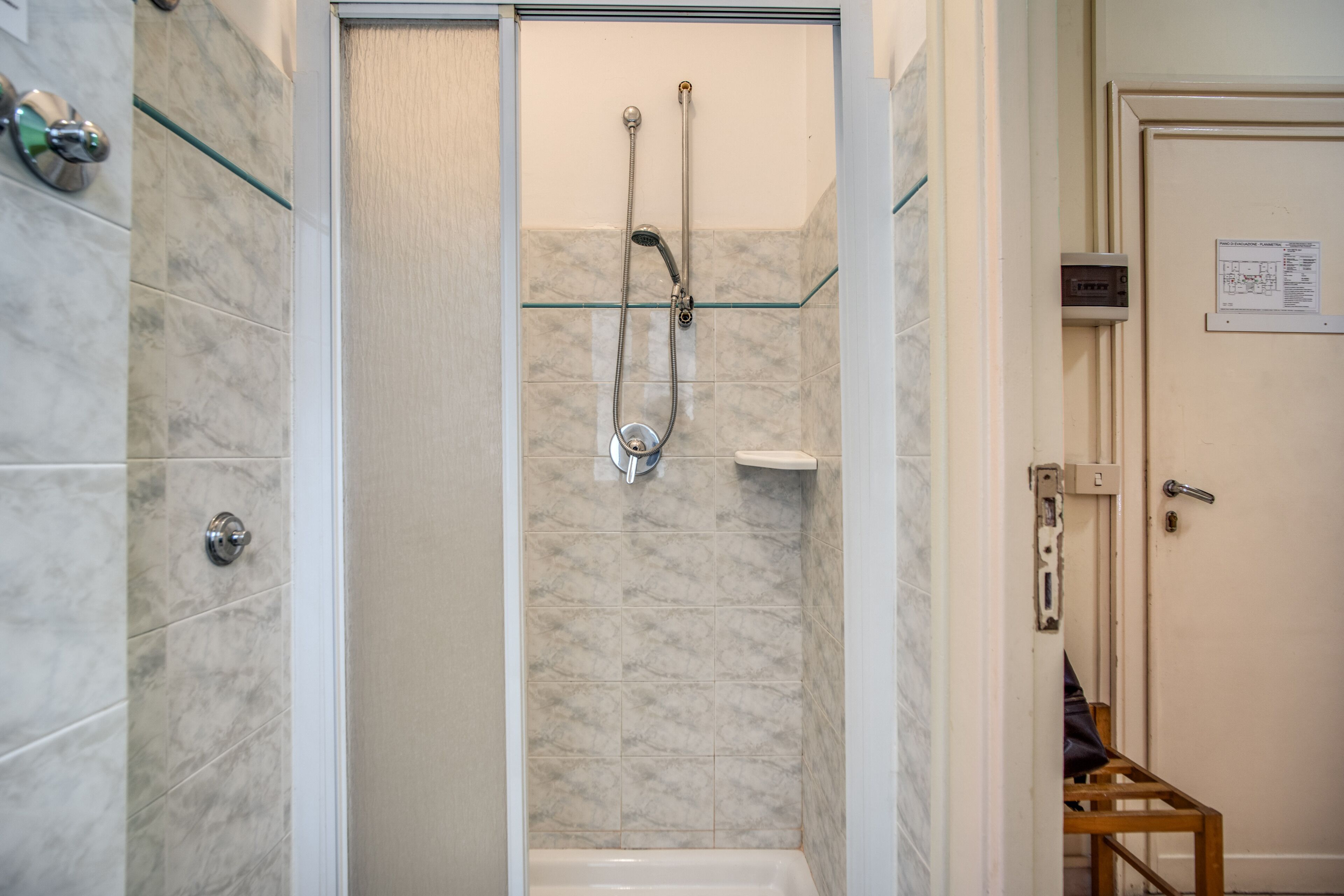 A walk-in shower with a glass door, marble tiles, and a handheld showerhead.