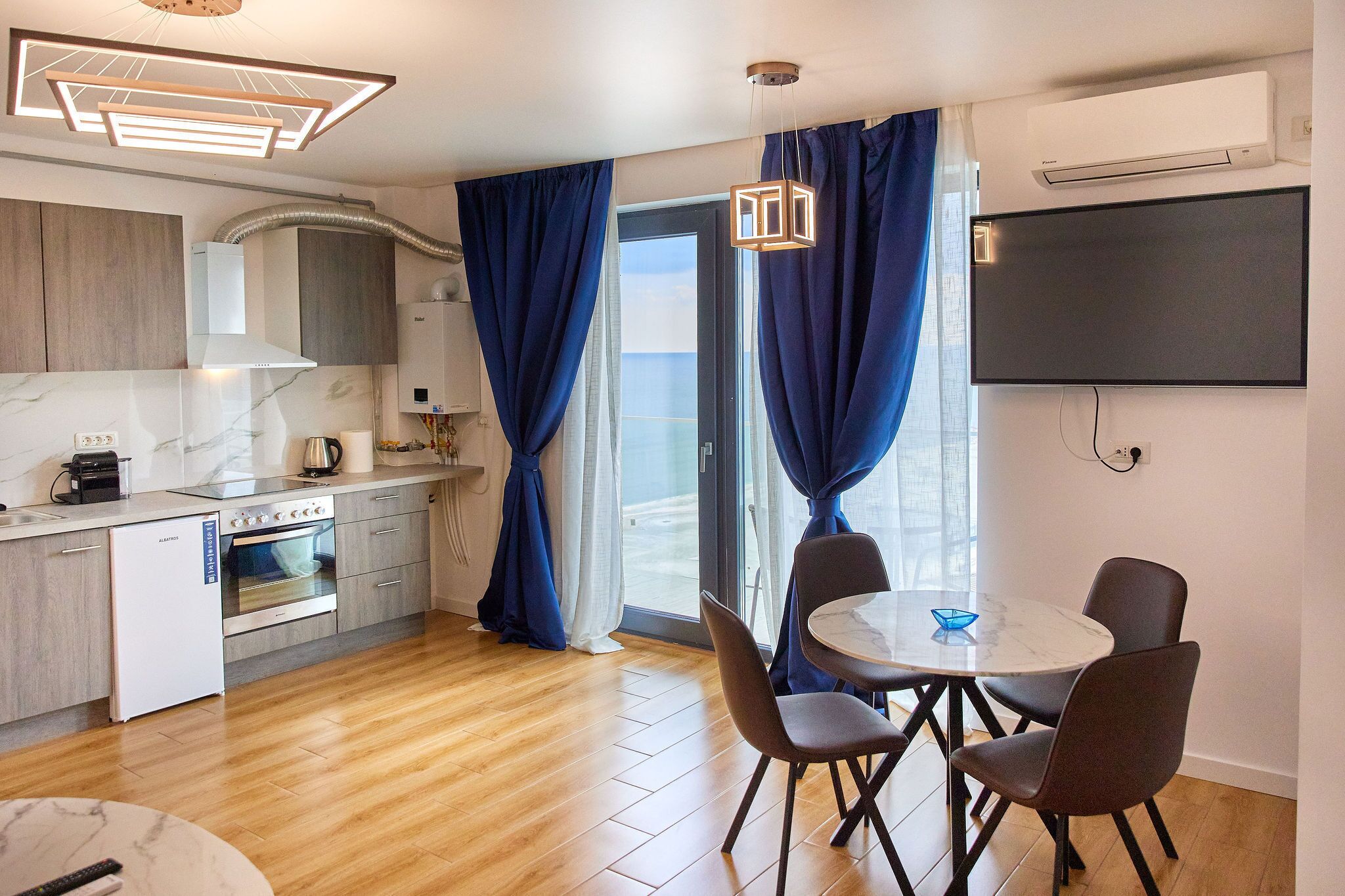 A modern kitchen with a built-in oven, a white refrigerator, and a dining area with a round table and four chairs.