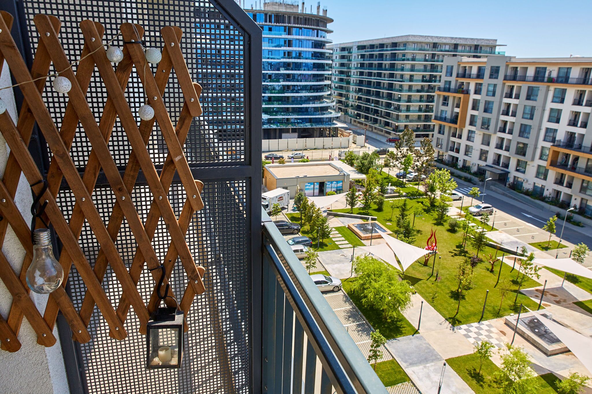 Un edificio moderno con un balcón, vistas a un patio ajardinado y edificios altos circundantes.