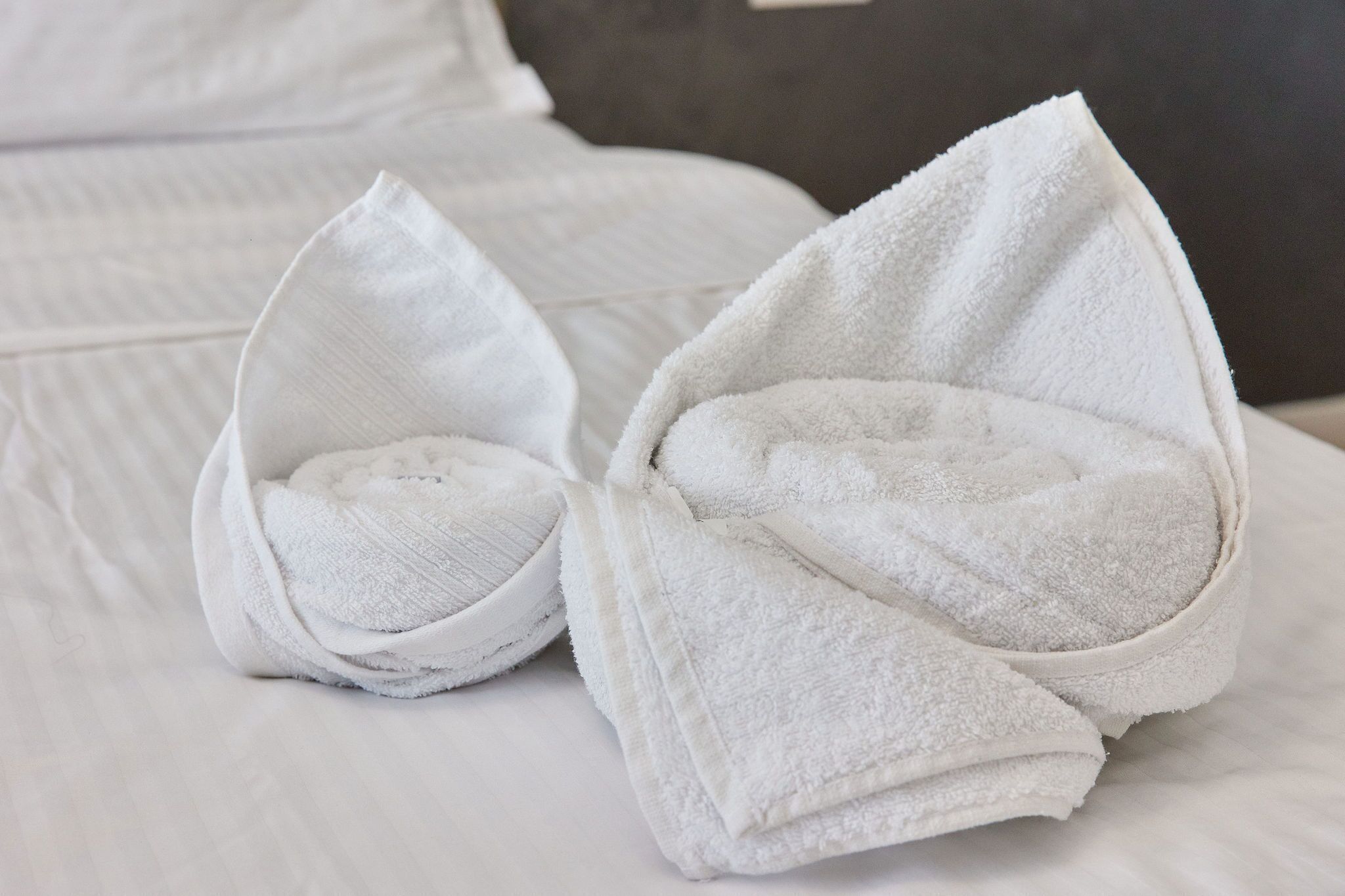 A neatly made bed with white linens and two towels folded into small, rounded shapes.
