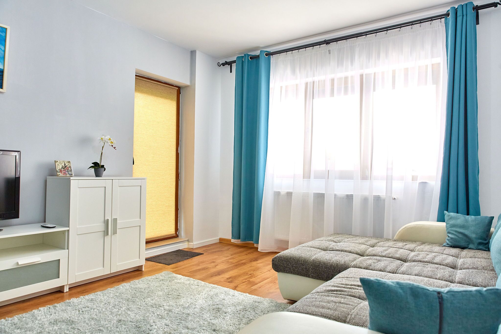 A modern bedroom with a bed, a TV, a wardrobe, and a window with curtains.