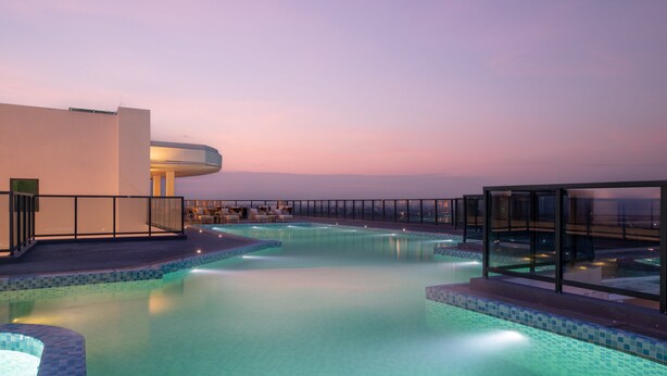 Une piscine à débordement située sur le toit, offrant une vue dégagée sur l’horizon, et entourée d’une architecture moderne et de chaises longues.