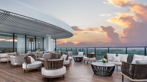Un salon sur le toit, doté d’un espace extérieur, de grandes fenêtres et offrant une vue sur les toits de la ville au coucher du soleil.