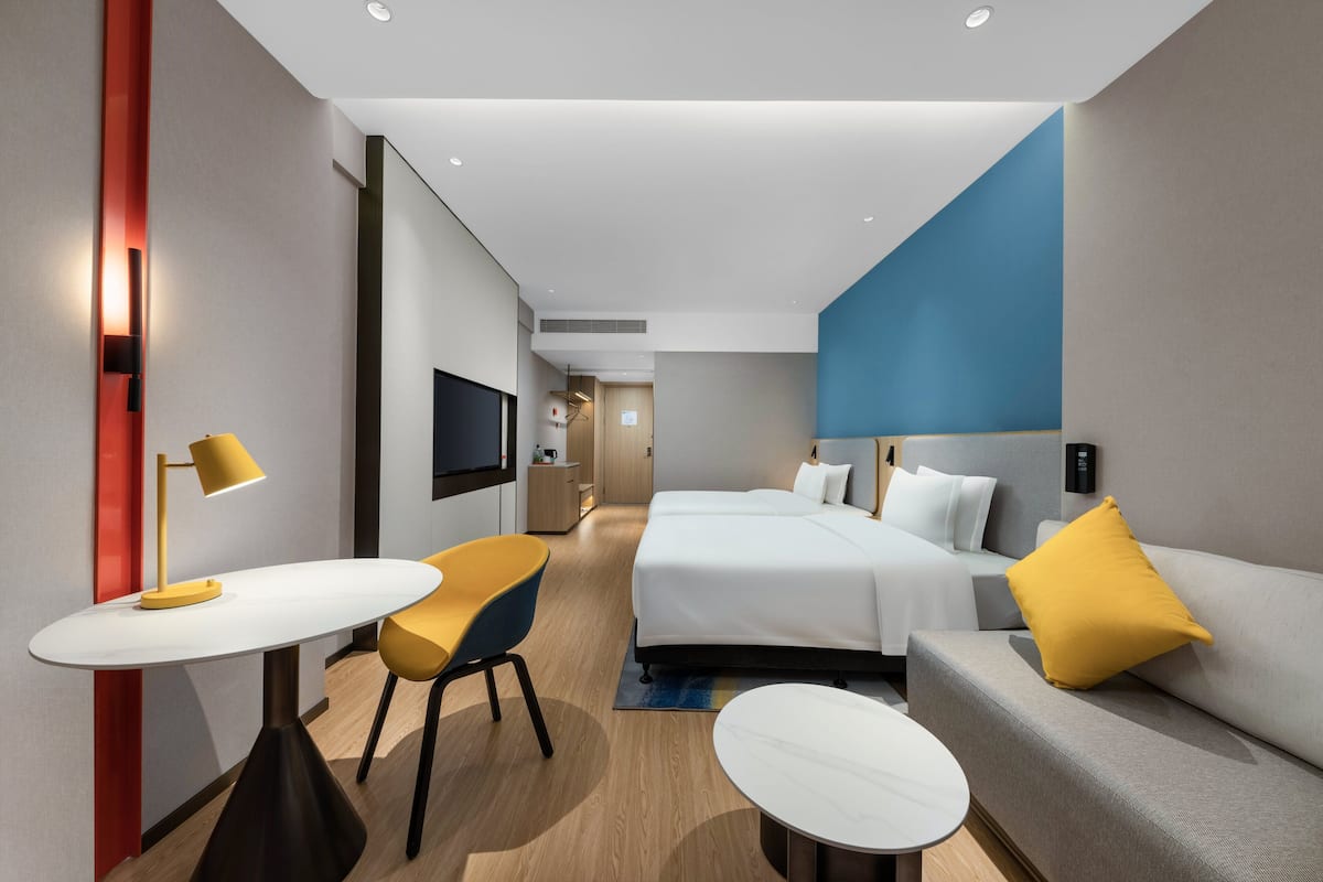 Una habitación de hotel moderna con cama, sofá y una pequeña mesa con lámpara.