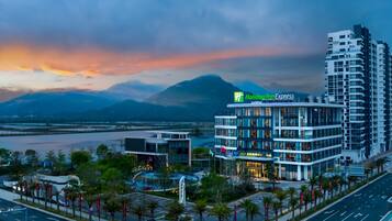 Un hôtel Holiday Inn Express au design moderne, situé près d’un plan d’eau, avec des montagnes en arrière-plan.