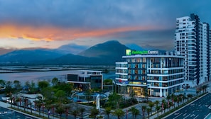 A Holiday Inn Express hotel with a modern design, located near a body of water with mountains in the background. - Holiday Inn Express Jiangmen Yinhu Bay by IHG (Jiangmen)