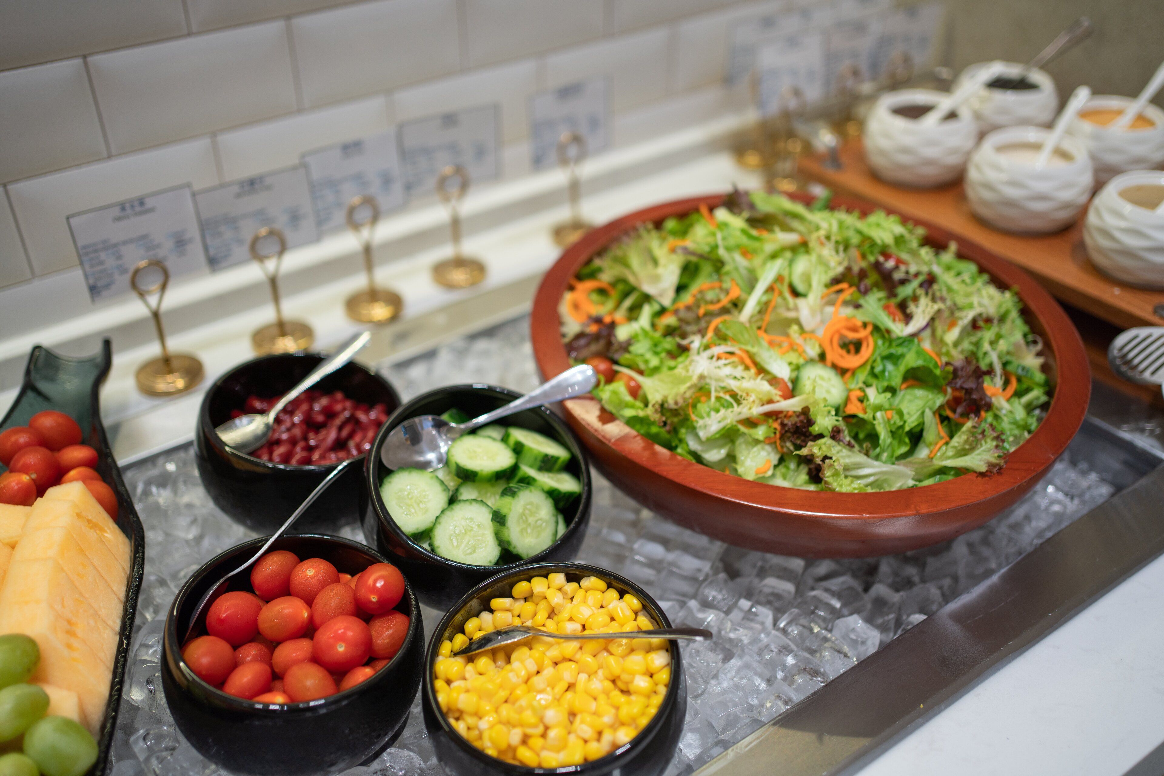 Un bufé con diversos alimentos, como tomates, pepinos, maíz y un gran bol de ensalada.