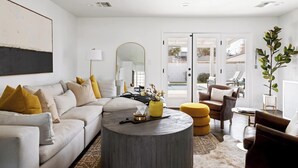 Un salon moderne avec un canapé, une table basse et des fauteuils. On y trouve un grand miroir, une lampe et une plante.
