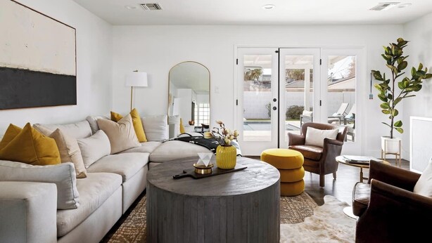 Un salon moderne avec un canapé, une table basse et des fauteuils. On y trouve un grand miroir, une lampe et une plante.