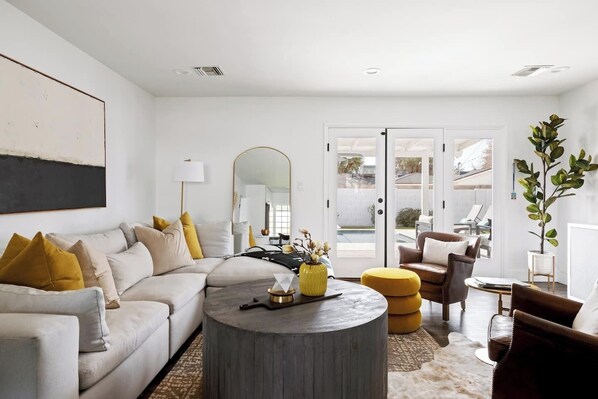 A modern living room with a sofa, coffee table, and chairs. There is a large mirror, a lamp, and a plant. - 8 Min to Old Town | 2 Master Suites | Heated Pool | Best Location | Sleeps 10 (Phoenix)