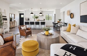 A spacious living room with a sofa, ottoman, and leather chair, a dining area with a table and chairs, and a kitchen with bar stools. - 8 Min to Old Town | 2 Master Suites | Heated Pool | Best Location | Sleeps 10 (Phoenix)