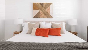 Une chambre à coucher bien aménagée, avec un grand lit, deux tables de chevet dotées de lampes et une œuvre d’art aux motifs géométriques accrochée au mur.