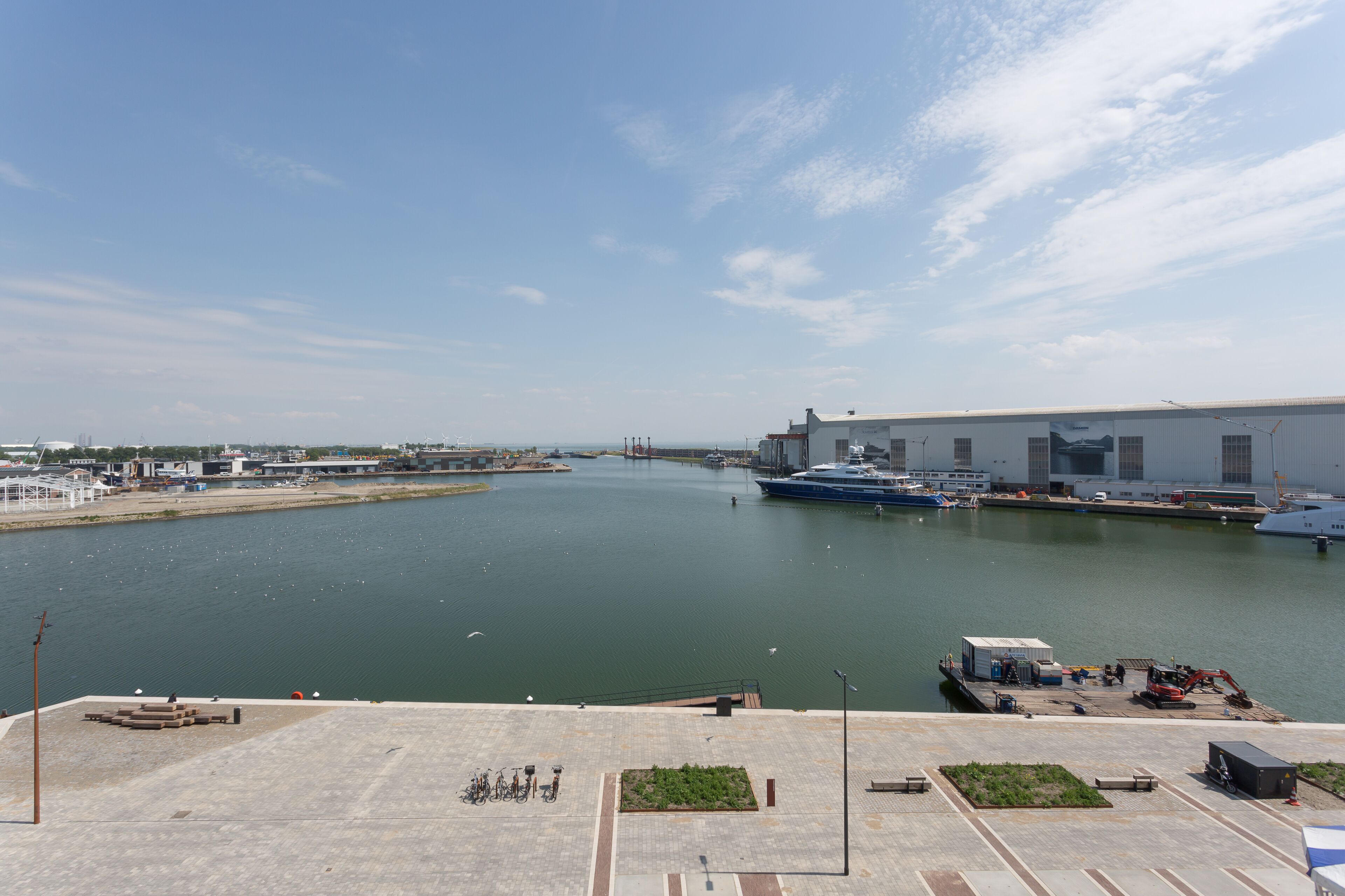 A marina with boats docked, a large industrial building, and a clear sky.