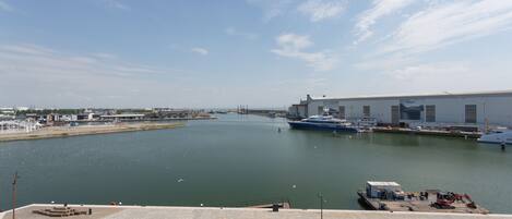 A marina with boats docked, a large industrial building, and a clear sky.