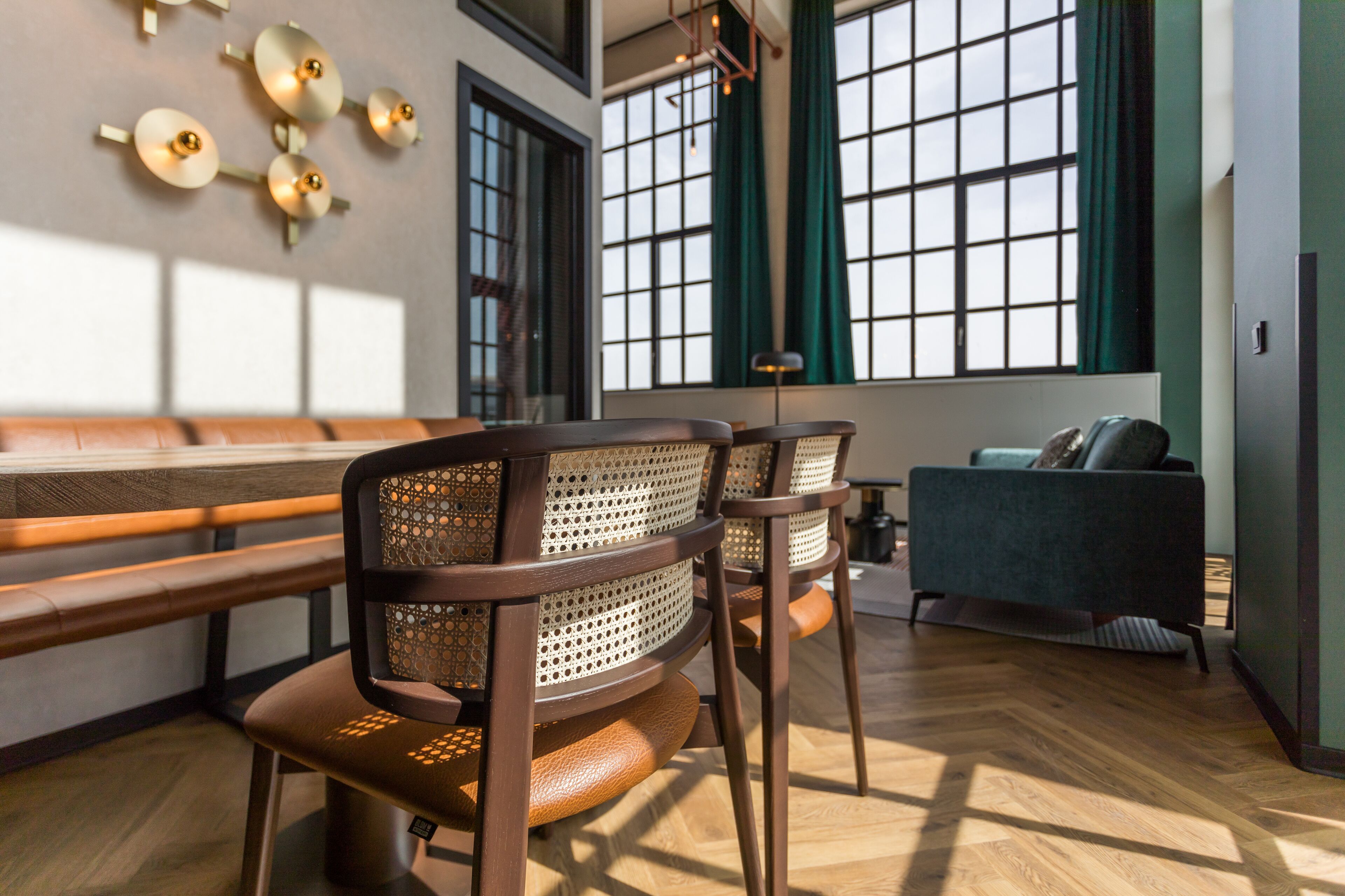 Un interior moderno con un banco de madera, dos sillones tapizados, un sofá y un ventanal con cortinas.