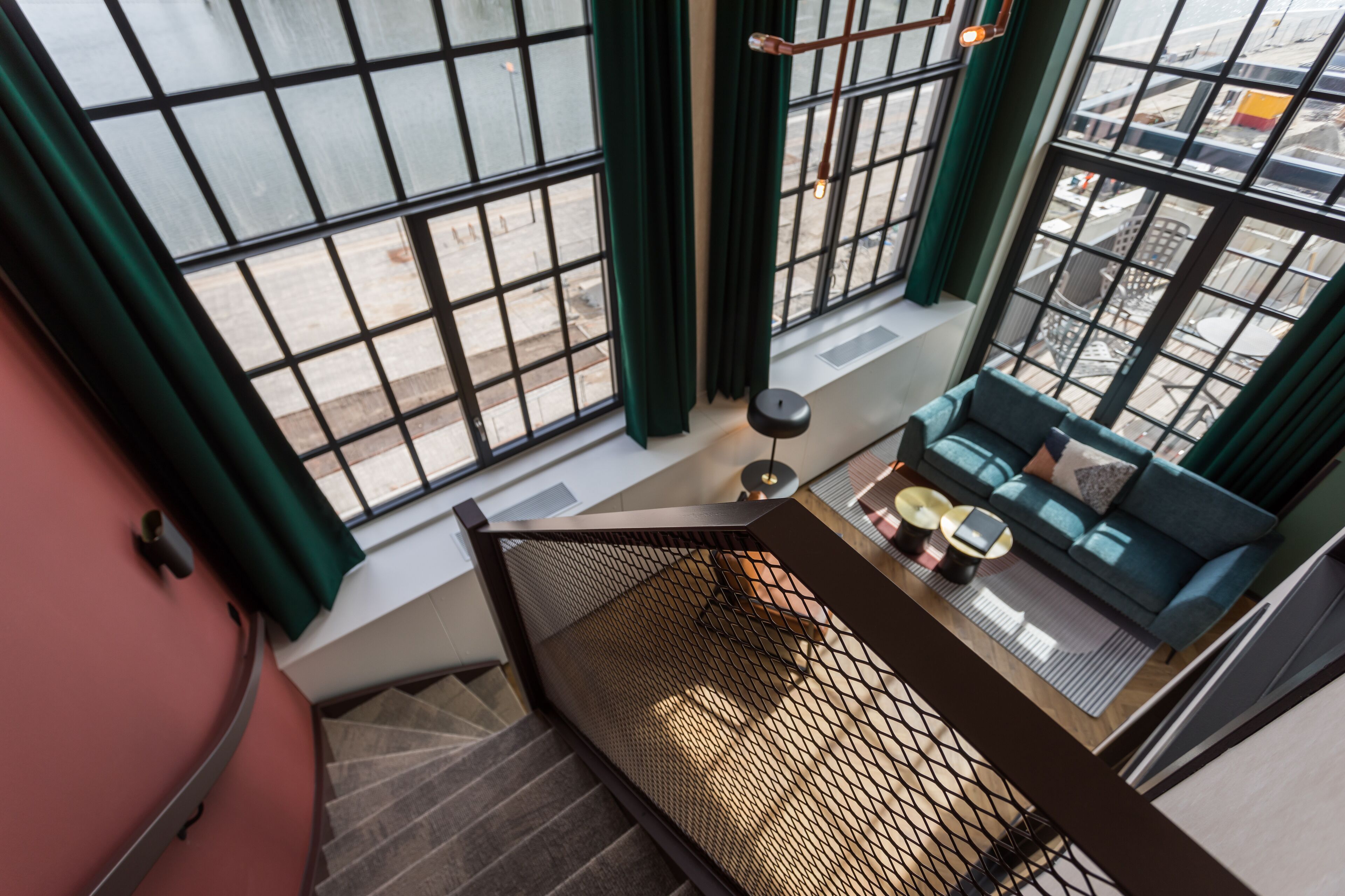 Ein Hochhaus-Interieur mit einer Treppe, die zu einem Balkon führt, einem blauen Sofa und einem Tisch mit zwei Lampen.
