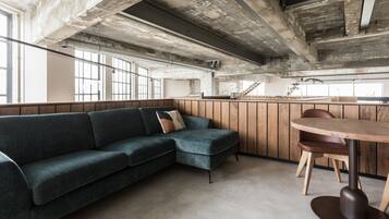 Un interior moderno con un sofá modular, una mesa redonda de madera y una escalera que sube a un nivel superior.