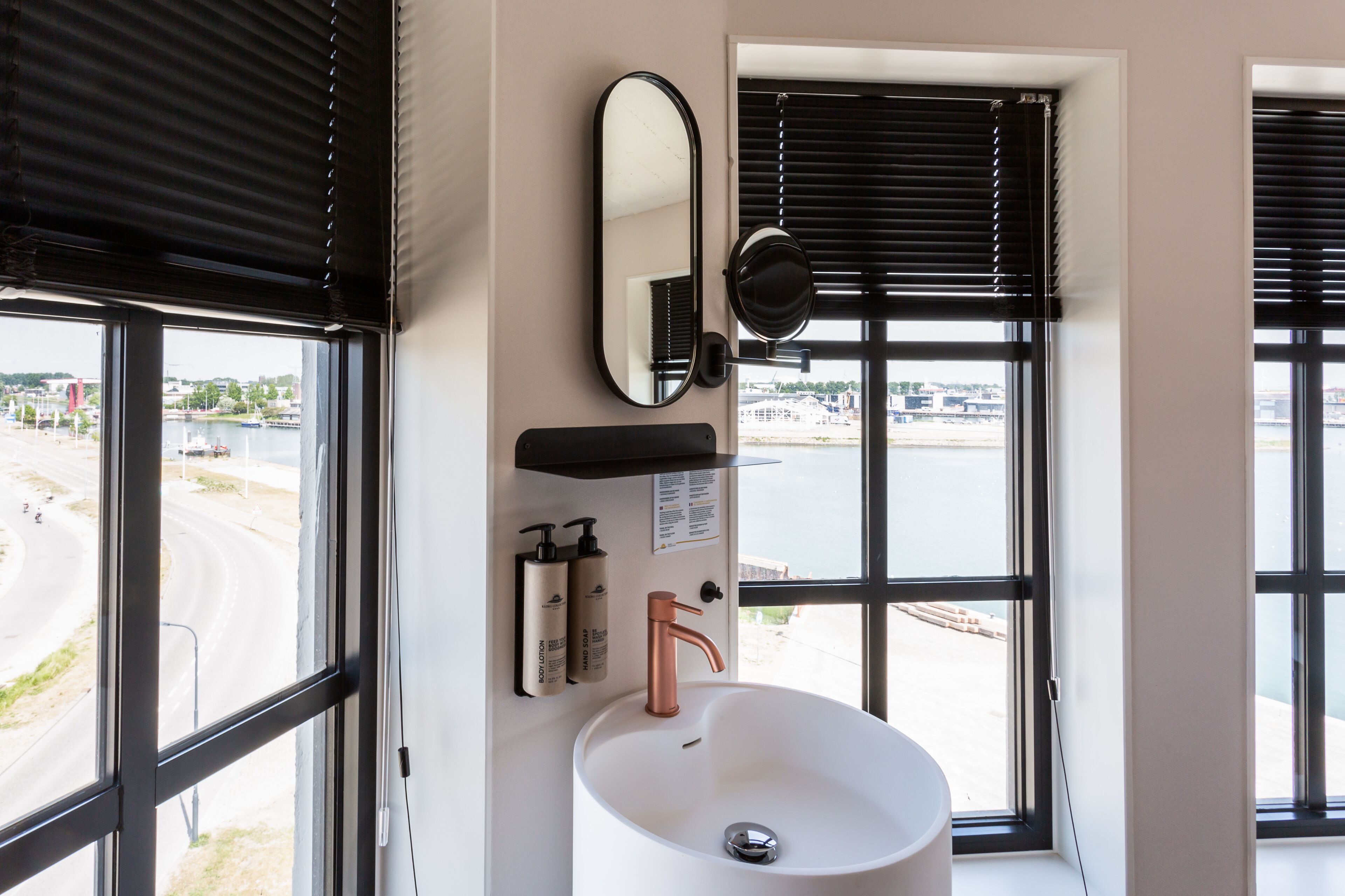 A bathroom with a white sink, a mirror, and two windows with black blinds.