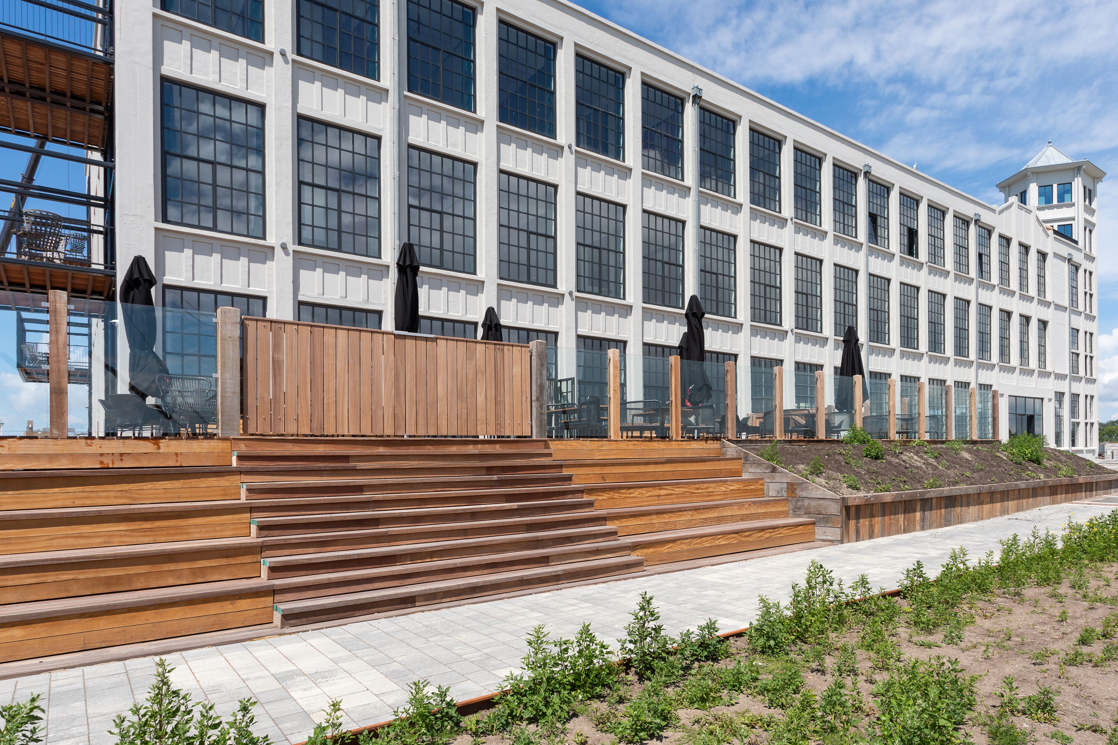 Een modern gebouw met grote ramen en een houten trap die naar een terras leidt.