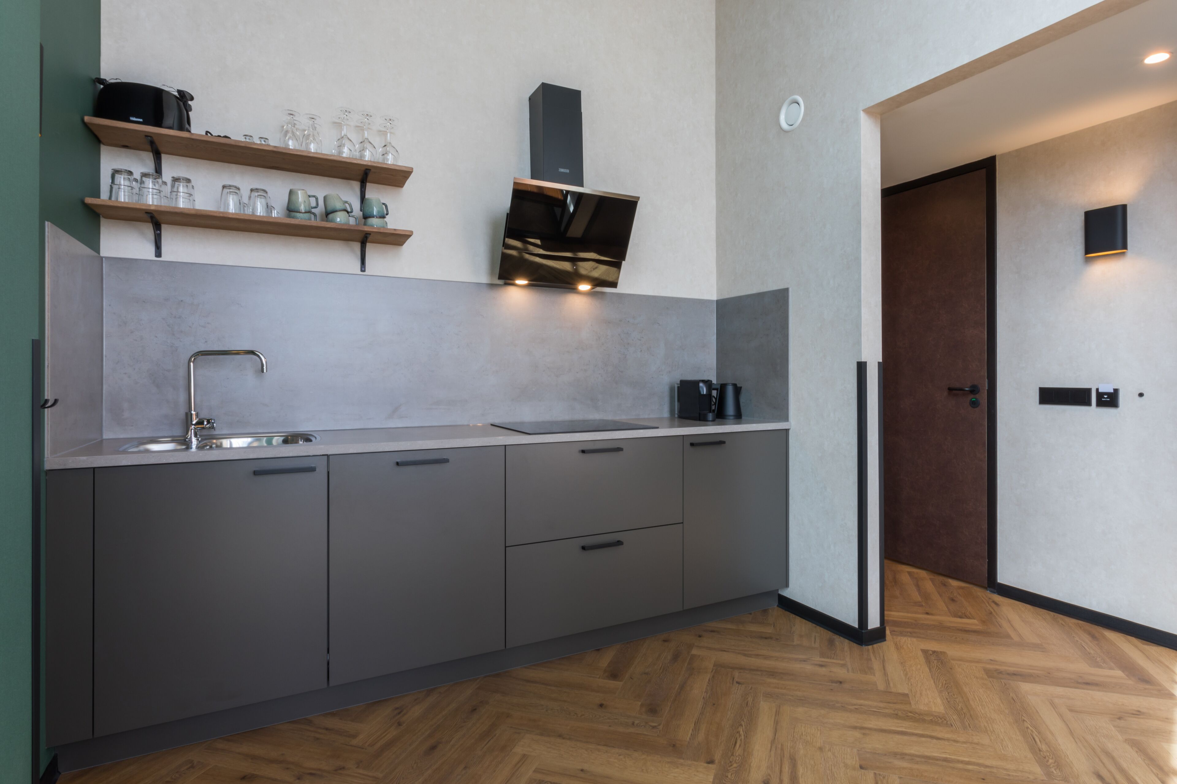 A modern kitchen with grey cabinets, a stainless steel sink, and wooden shelves above.