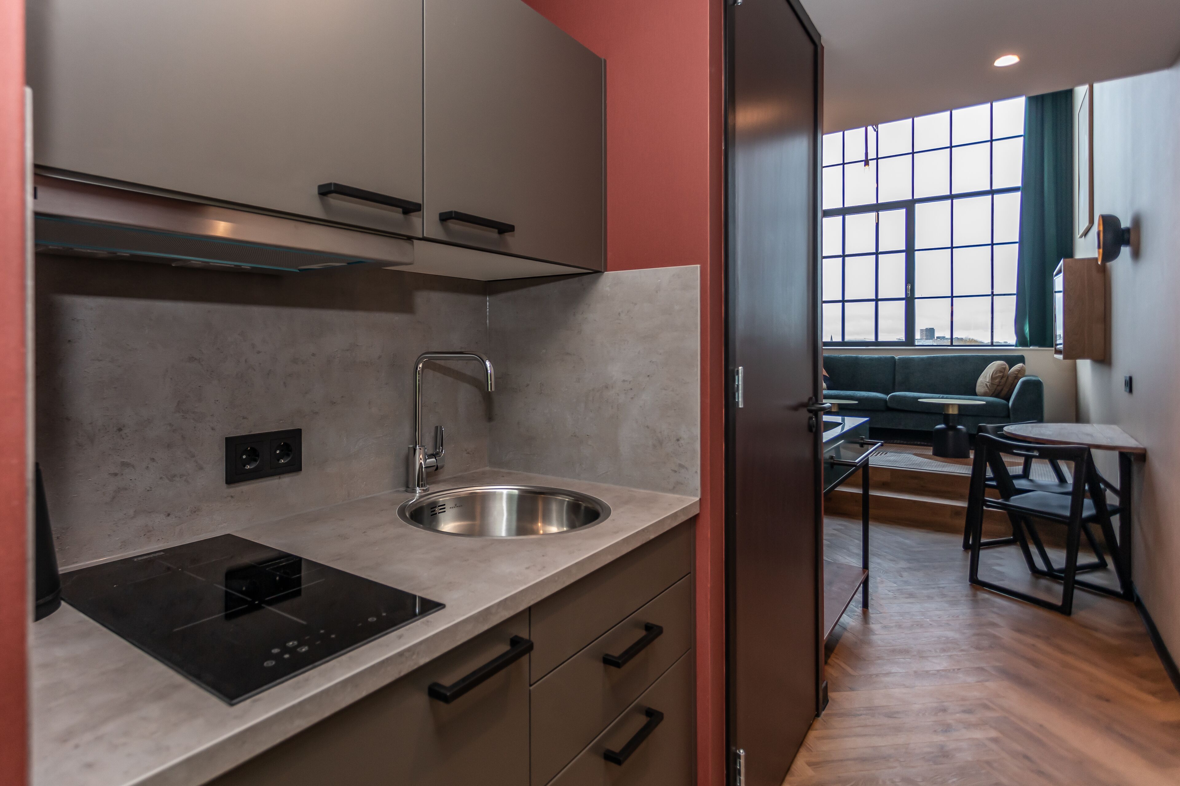 A modern kitchen with a built-in stove, sink, and cabinets, leading to a living area with a sofa and a table.