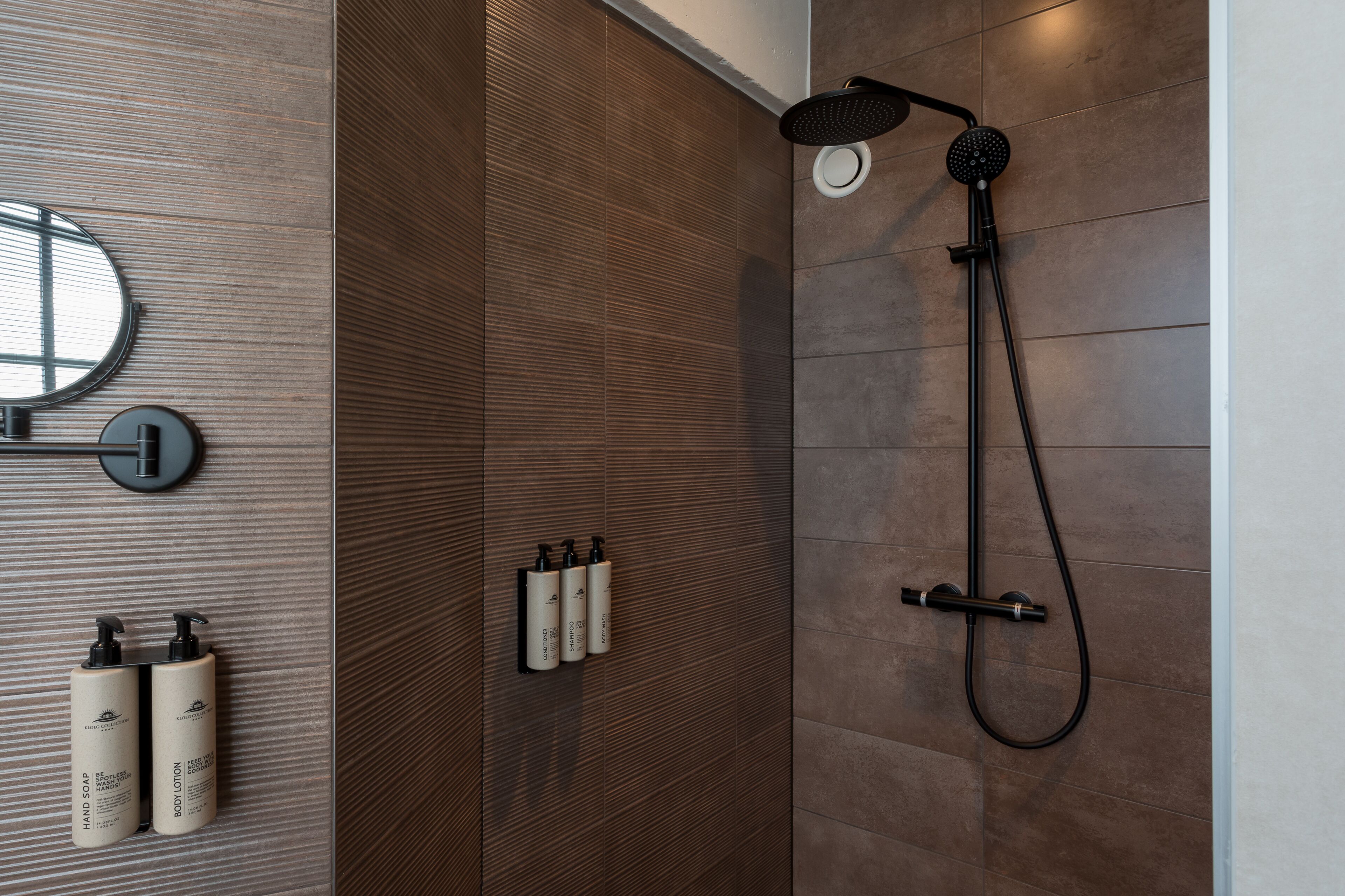 A modern bathroom with a shower, a mirror, and two bottles of shampoo and lotion.