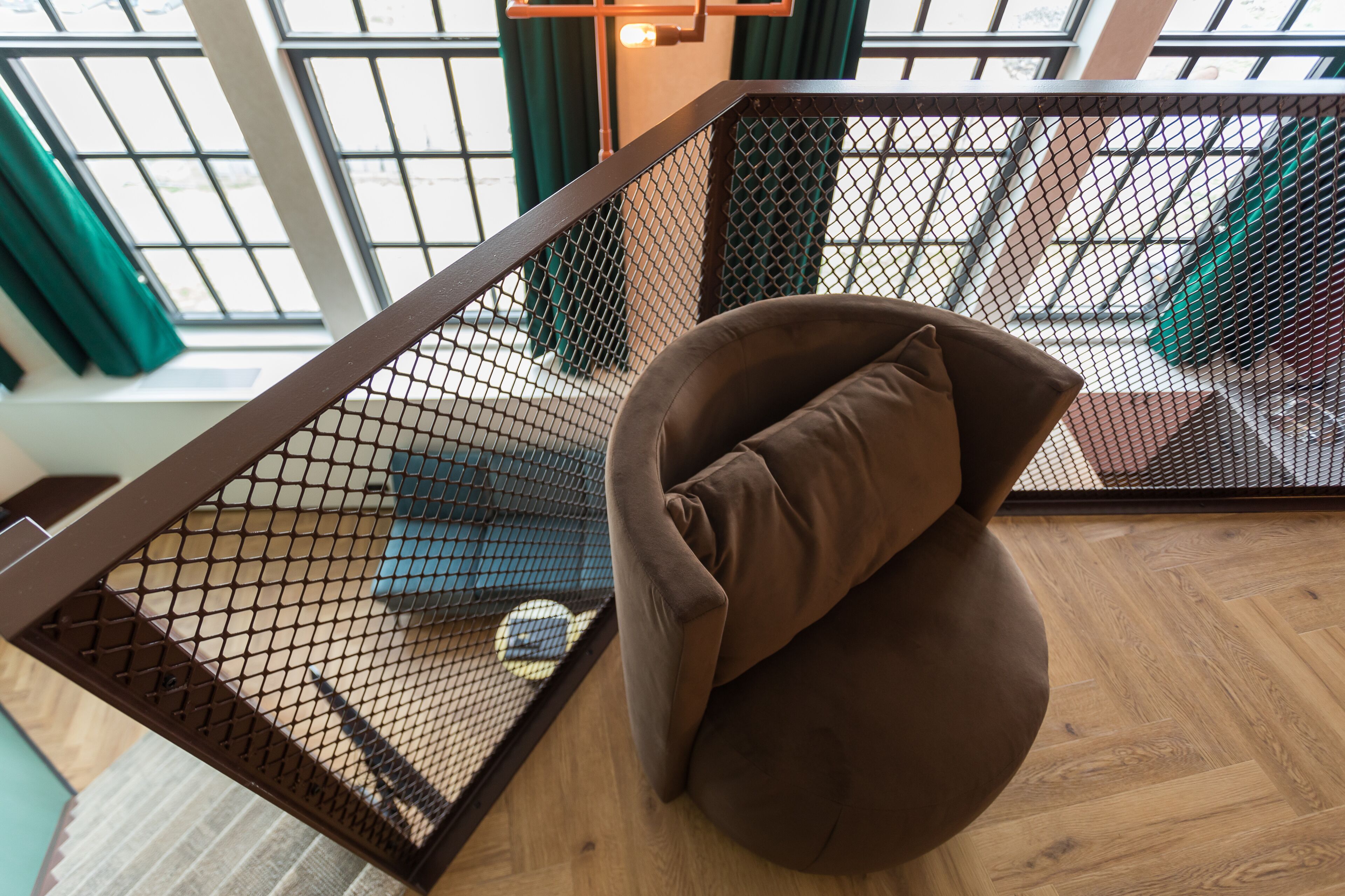 A modern interior with a brown cushioned chair, a wooden floor, and a metal railing with a mesh design.