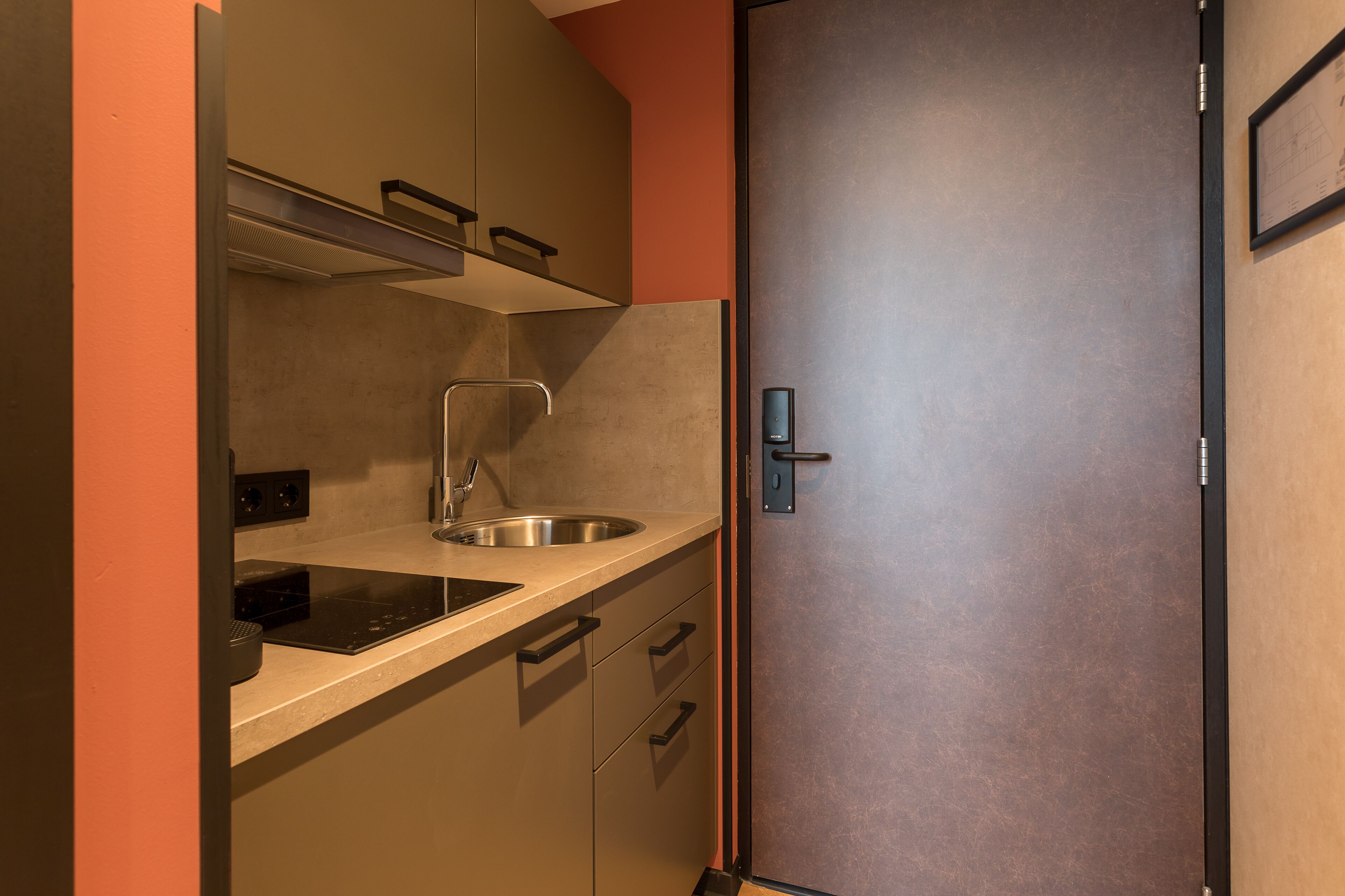 A compact kitchen with a stainless steel sink, a built-in oven, and a door with a handle.