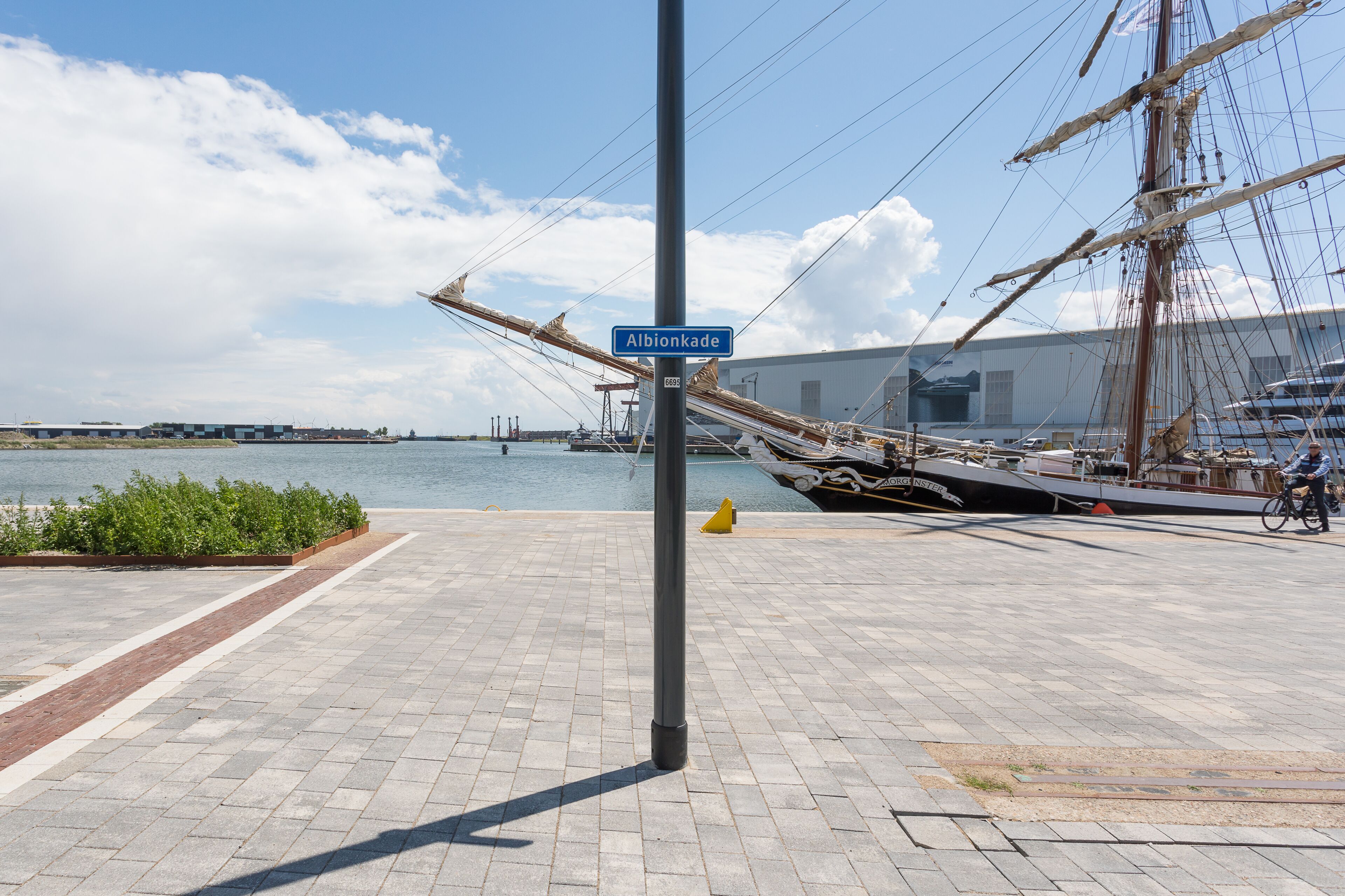 A paved waterfront promenade with a tall ship docked nearby.