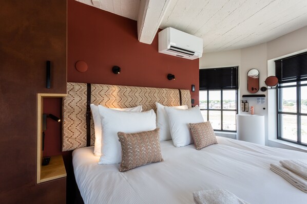 Una habitación de hotel moderna con una cama grande, cabecera estampada y vistas de la ciudad a través de amplios ventanales.