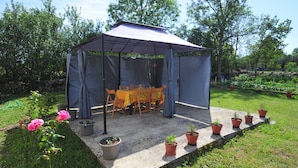 Een overdekt terras met een tafel en stoelen, omringd door potplanten en een tuin.