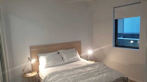 A bedroom with a bed, two bedside lamps, and a window with blinds. - Open 1 Bedroom Apartment in Brisbane City (Brisbane)