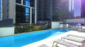 A swimming pool with lounge chairs, surrounded by a modern building with large windows. - Open 1 Bedroom Apartment in Brisbane City (Brisbane)