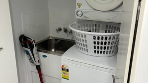 A compact laundry room with a washing machine, a dryer, and a mopping tool. - Open 1 Bedroom Apartment in Brisbane City (Brisbane)