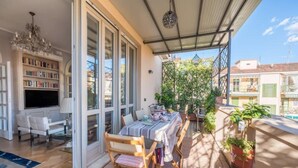 A sunlit patio with a dining table, chairs, and a bookshelf. - Lovely apartment with furnished terrace (Torino)