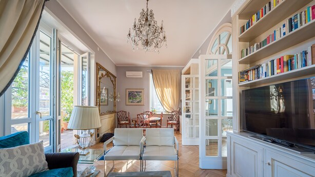 A spacious living room with a large TV, bookshelves, a chandelier, and a dining area. - Lovely apartment with furnished terrace (Torino)