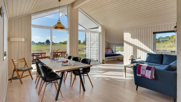 Amplia sala de estar con una gran mesa de comedor, un sofá azul y vistas a un campo verde a través de amplias ventanas.