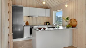 Una cocina moderna con paredes de madera, un refrigerador de acero inoxidable, armarios blancos, un ventanal grande y una isla central con un fregadero y recipientes.