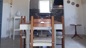 Un comedor con techo de arco de piedra, una mesa de madera con sillas, una lámpara colgante y vista a la cocina.