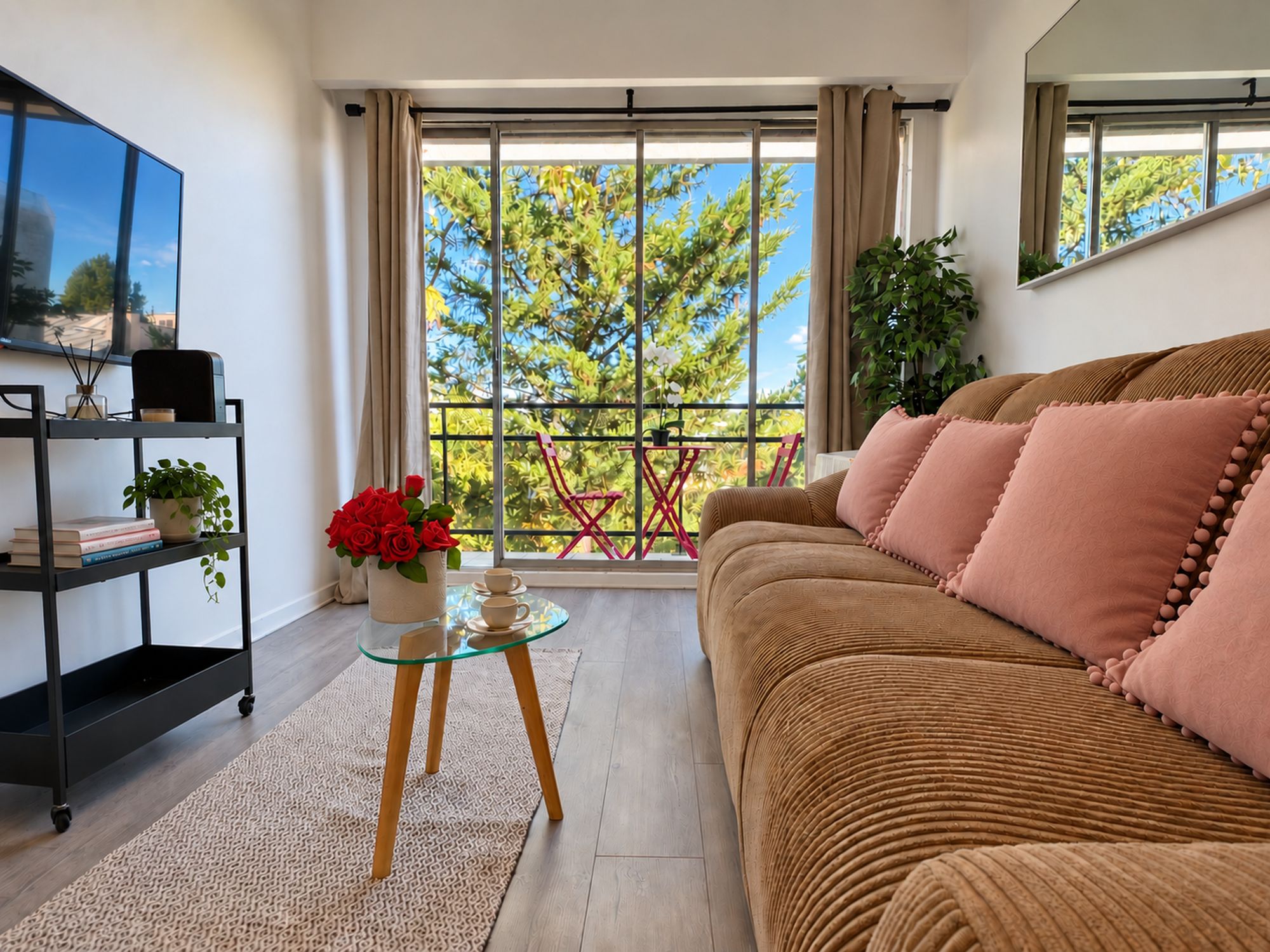 A modern living room with a sofa, a glass coffee table, a bookshelf, and a balcony with a view of trees.