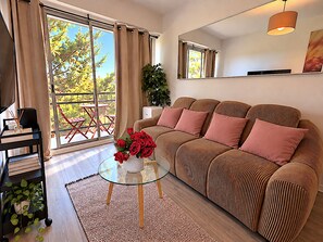 Un salon moderne avec un canapé, une table basse en verre et une vue sur un balcon agrémenté de chaises rouges.