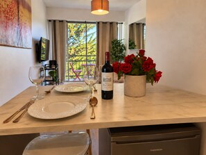 Un coin repas avec une table dressée pour deux personnes, une bouteille de vin et un vase de roses rouges.
