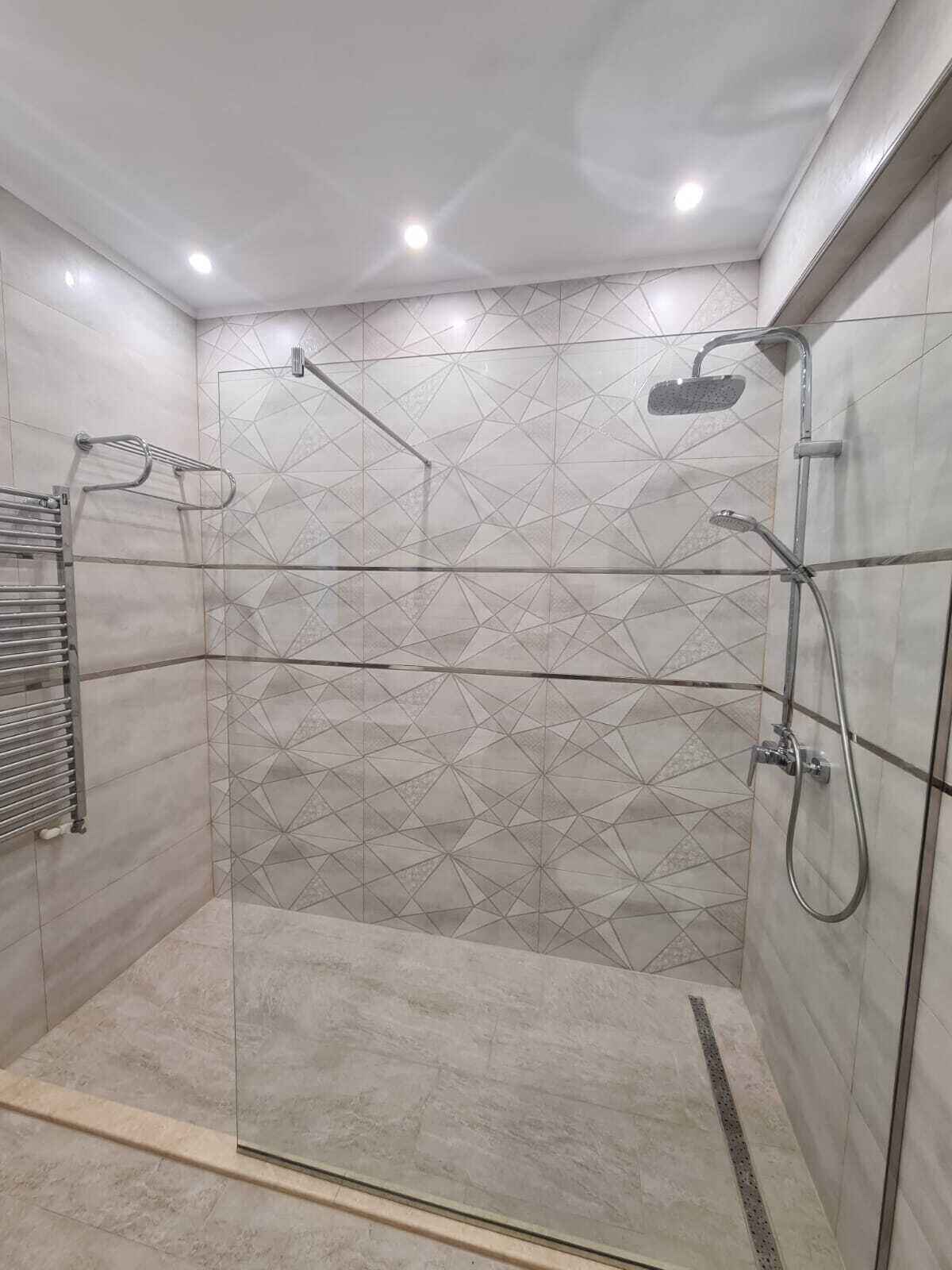 A modern shower with a geometric tile pattern, a glass door, and a metal towel rack.